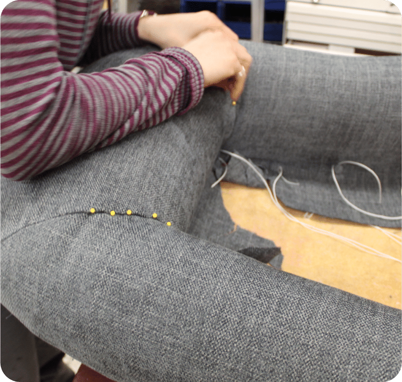 Gros plan sur un travail de couture. On voit les bras et mains de l'artisan exécuter une couture à la main