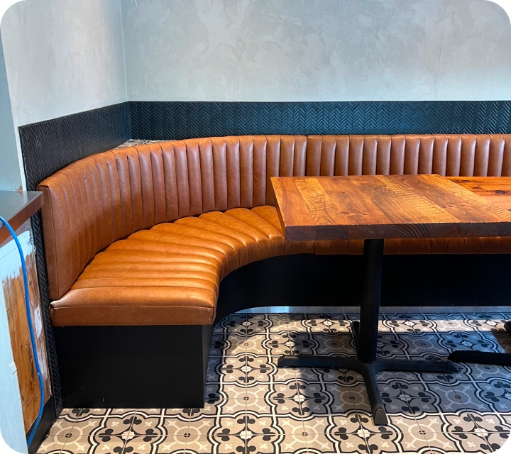 Partial side view of a restaurant dining room bench. The seat and back are made of padded and assembled flutes (tubes). Rounded corner. Caramel-colored faux leather. Bench custom-made according to customer choices and preferences. Réno-Montréal collaboration