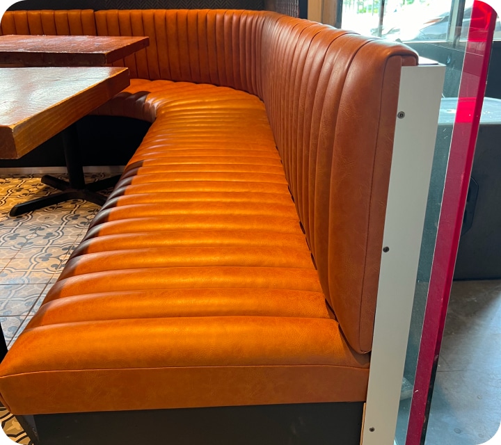 Partial side view of a restaurant dining room bench. The seat and back are made of padded and assembled flutes (tubes). Rounded corner. Caramel-colored faux leather. Bench custom-made according to customer choices and preferences. Réno-Montréal collaboration