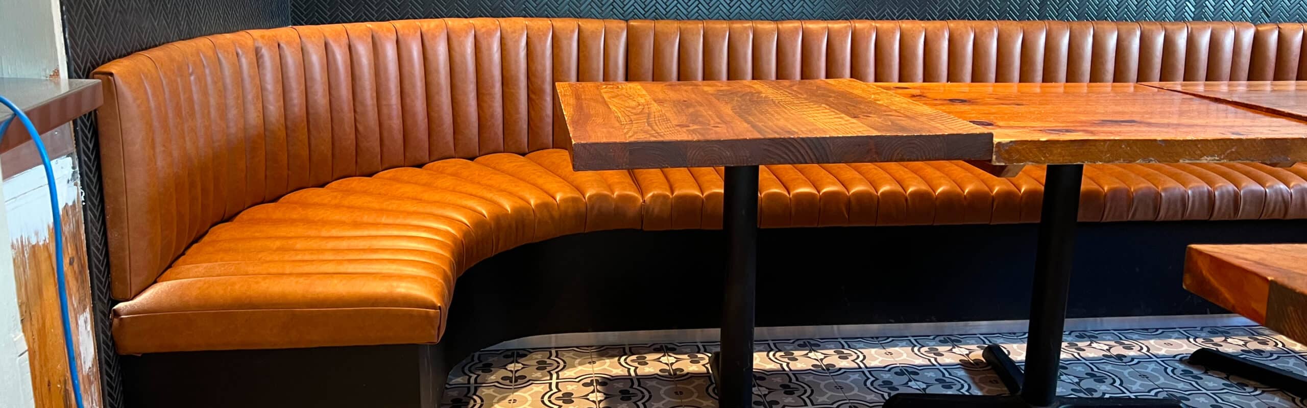Partial side view of a restaurant dining room bench. The seat and back are made of padded and assembled flutes (tubes). Rounded corner. Caramel-colored faux leather. Bench custom-made according to customer choices and preferences. Réno-Montréal collaboration