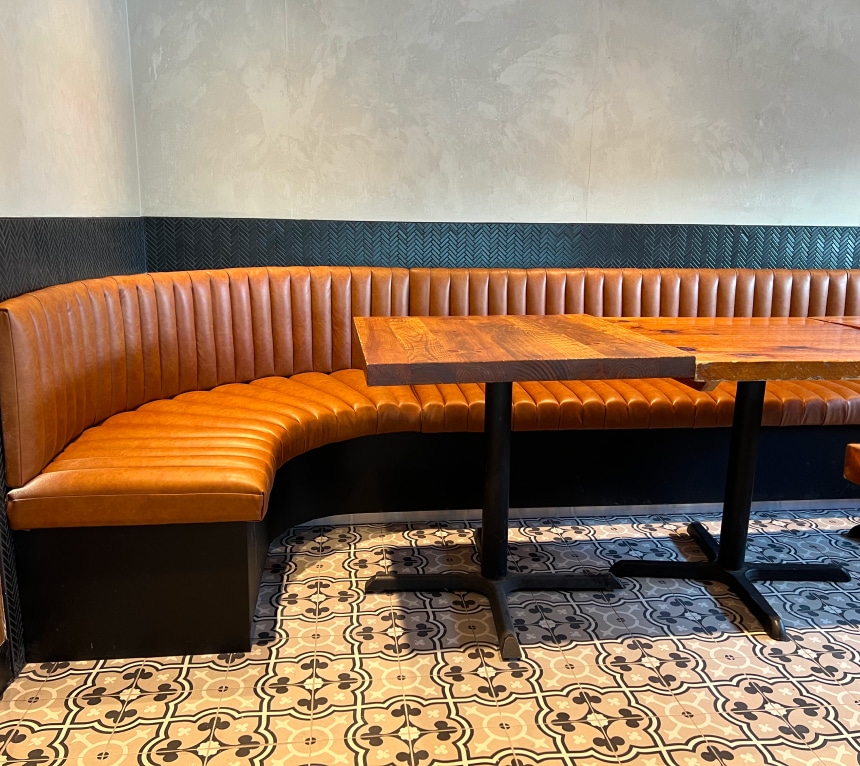 Partial side view of a restaurant dining room bench. The seat and back are made of padded and assembled flutes (tubes). Rounded corner. Caramel-colored faux leather. Bench custom-made according to customer choices and preferences. Réno-Montréal collaboration